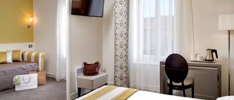 Una habitación de hotel con cama, escritorio, silla, televisor y ventana con cortinas.