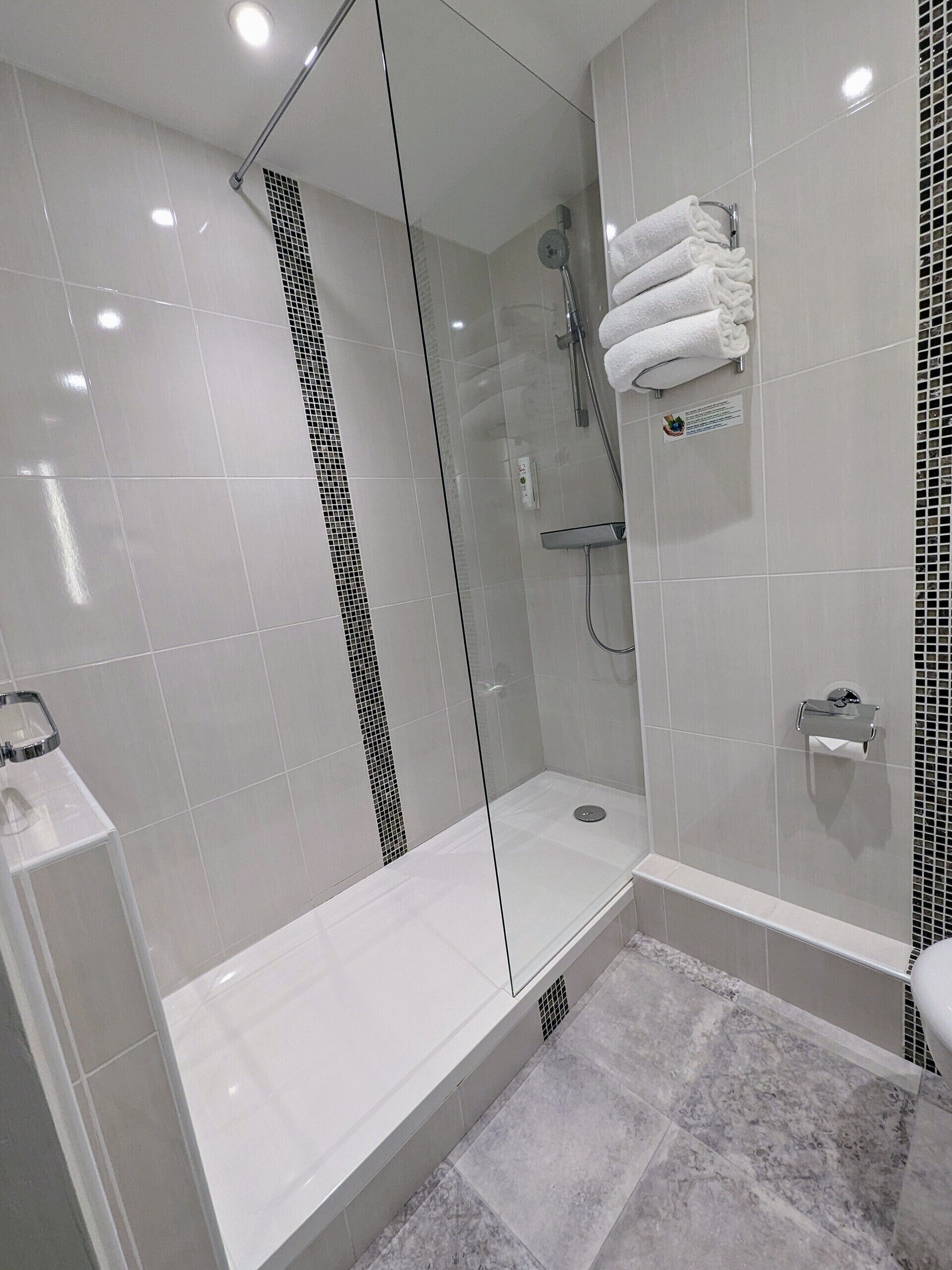 A modern bathroom with a glass-enclosed shower, white tiles, and a marble floor.