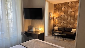 A hotel room with a bed, a desk with a lamp, a sofa, and a TV mounted on the wall. - HOTEL ARVERNA VICHY - ClT'HOTEL (Vichy)