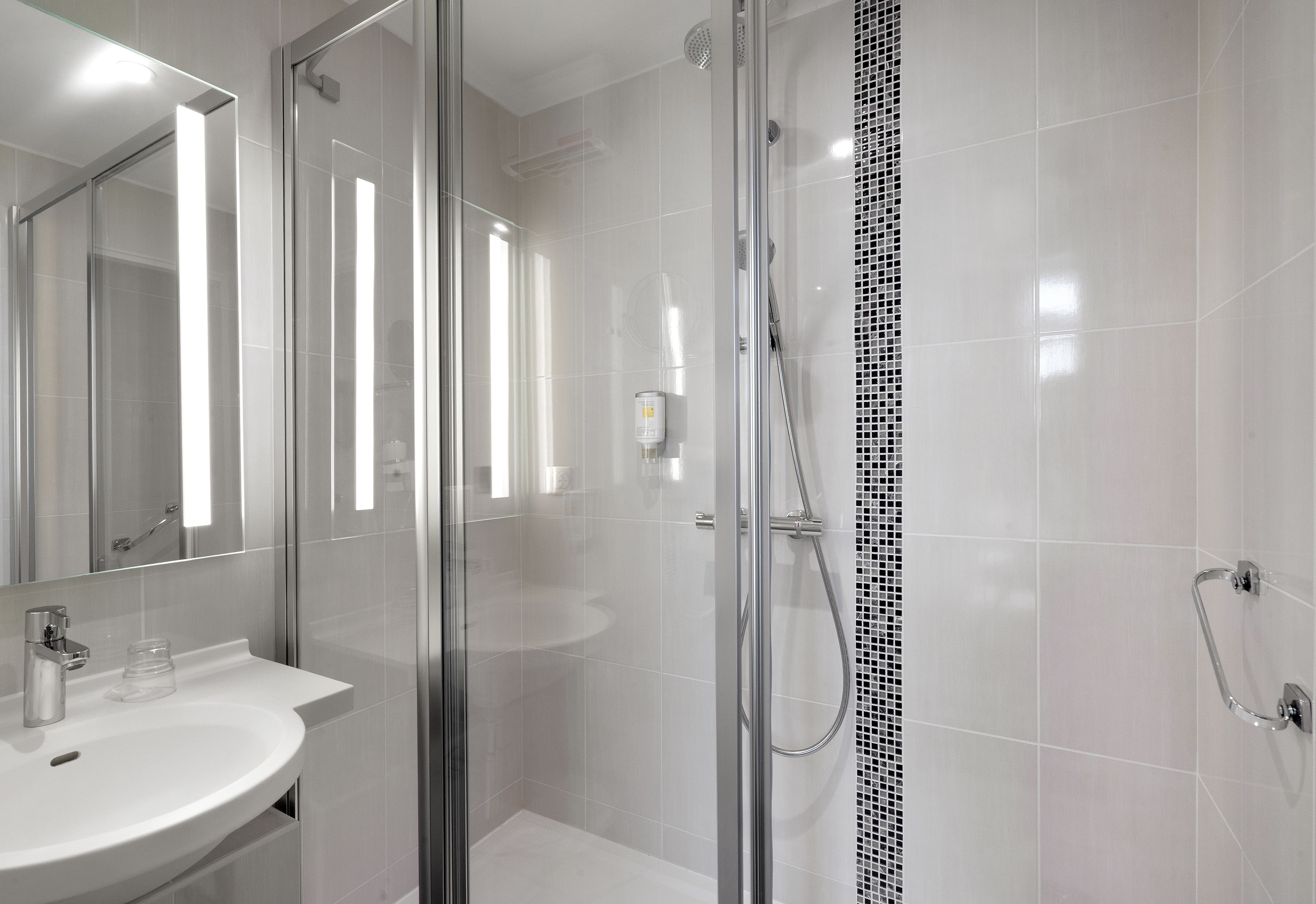 Un baño moderno con cabina de ducha de vidrio, lavamanos blanco y un espejo grande.