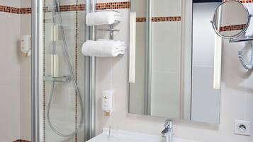 Un baño moderno con ducha envuelta en vidrio, un lavamanos blanco y un espejo.