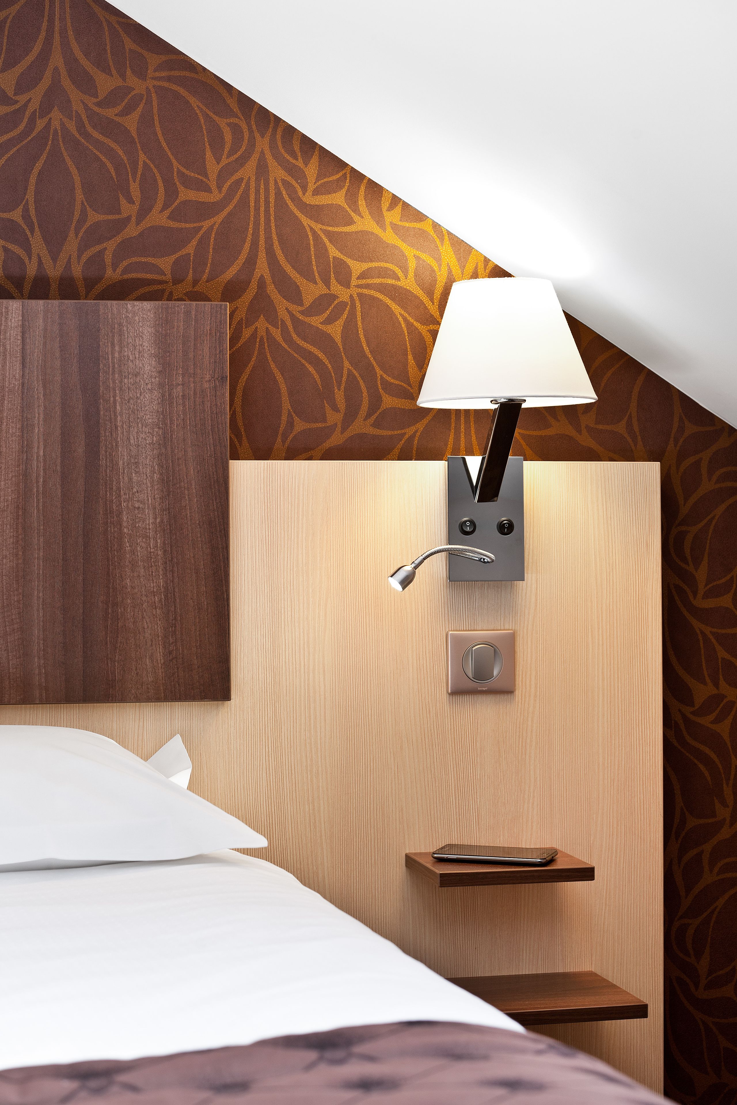 Ein Hotelzimmer mit einem Bett, einer Wandlampe und einem Regal mit einem Tablet.