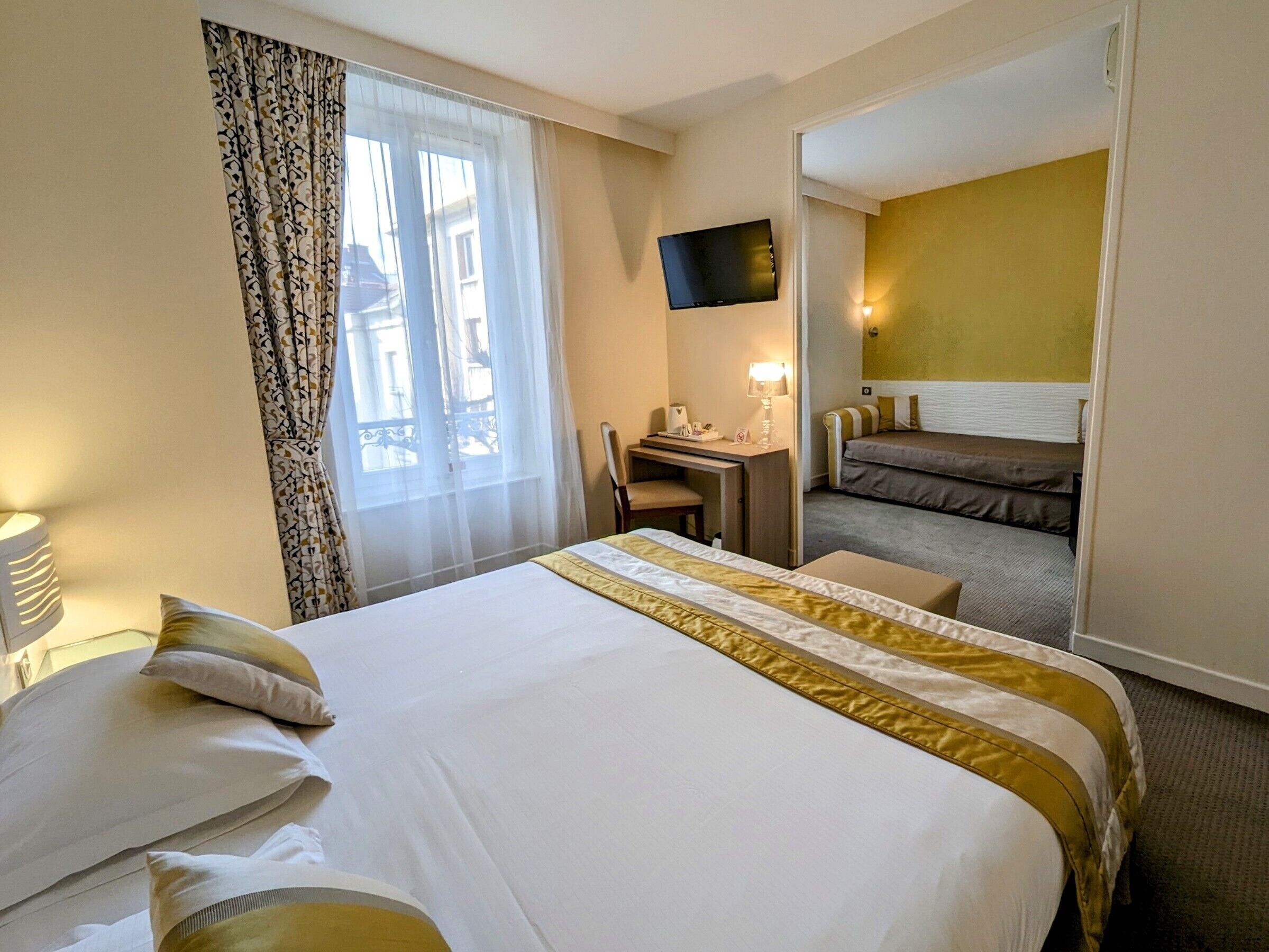 Habitación de hotel con una cama grande, un escritorio con silla, televisión y vistas al exterior.