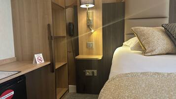 Une chambre d’hôtel équipée d’un lit, d’un bureau, d’un téléphone et d’une lampe fixée au mur.