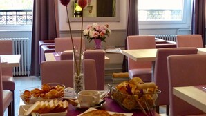 Un comedor con mesas y sillas, un florero con flores, y una ventana con cortinas.