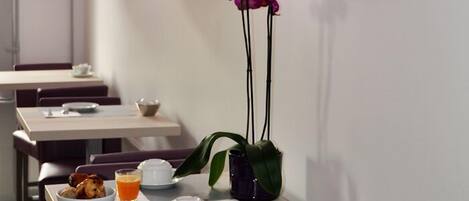 Un espace repas moderne avec des chaises violettes, une table où sont disposés des aliments pour le petit-déjeuner et des suspensions violettes.