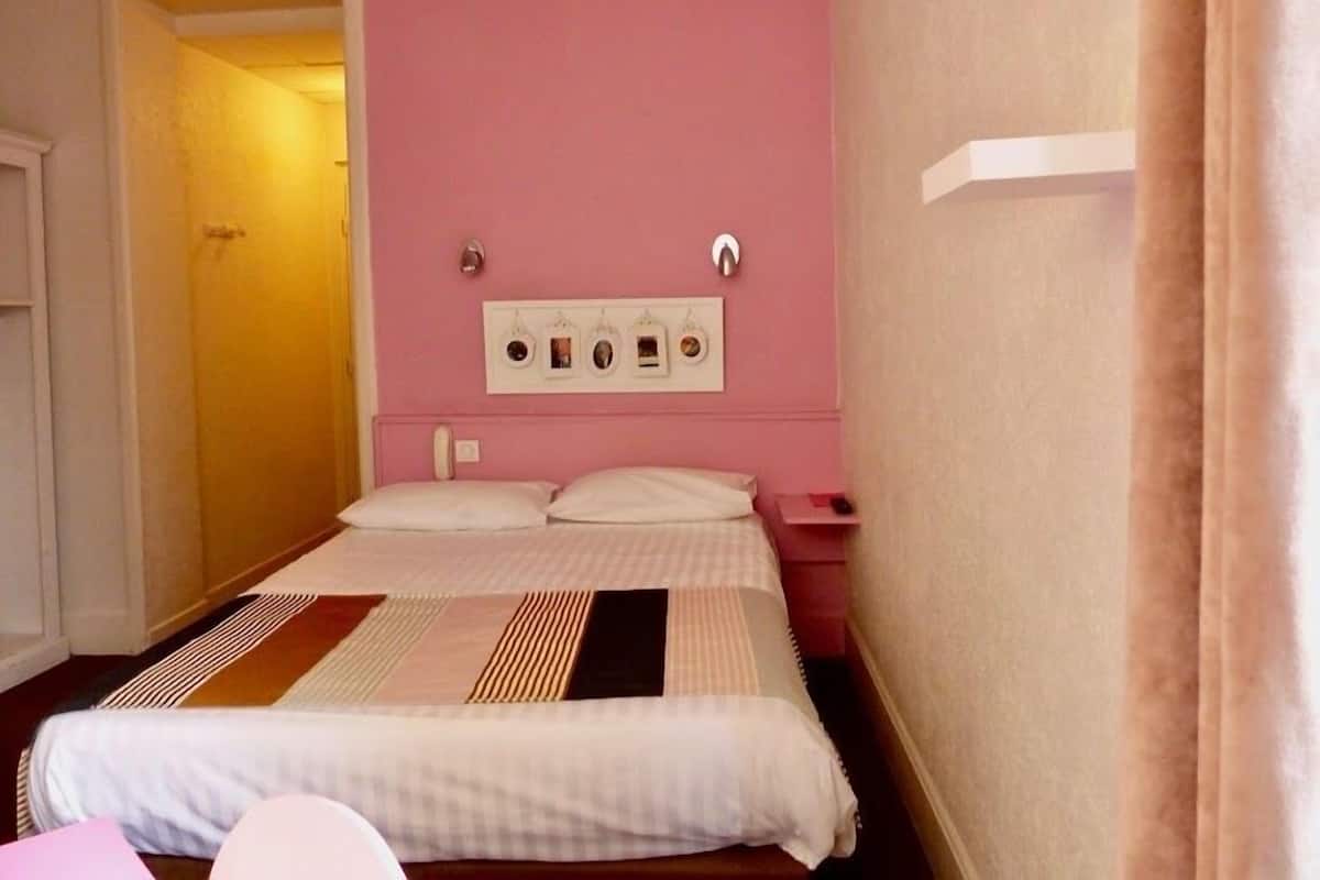 A single bed with a patterned bedspread, a bedside table, and a wall-mounted electrical outlet.