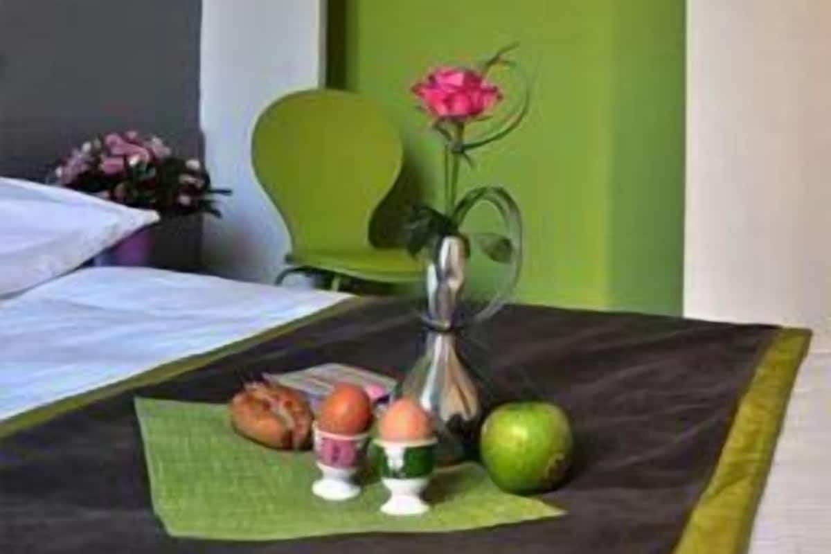 A neatly arranged hotel room with a bed, a green chair, a small table with a vase of flowers, and a green mat.