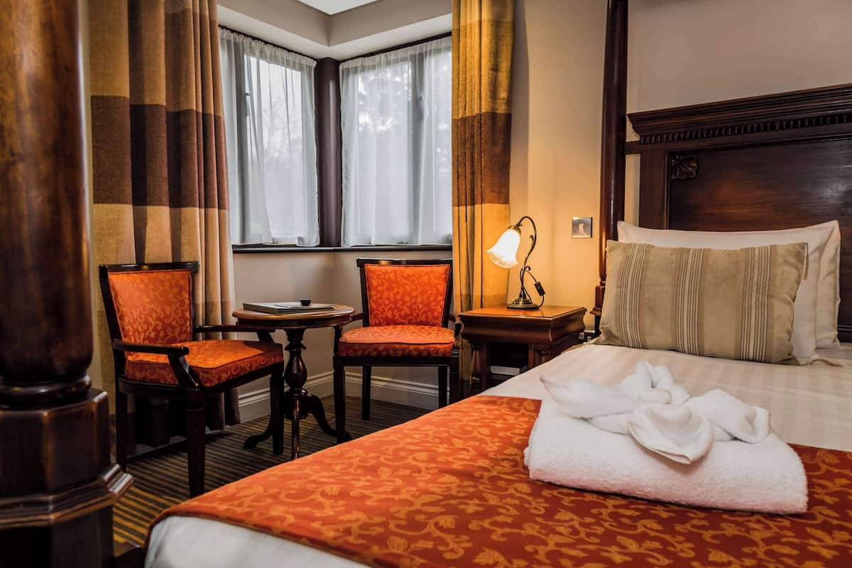 A hotel room with a large bed, two chairs, a small table, and a lamp.