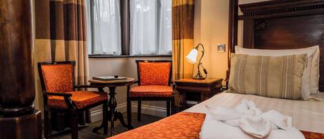 Habitación de hotel con una cama grande, dos sillas, una mesita y una lámpara.