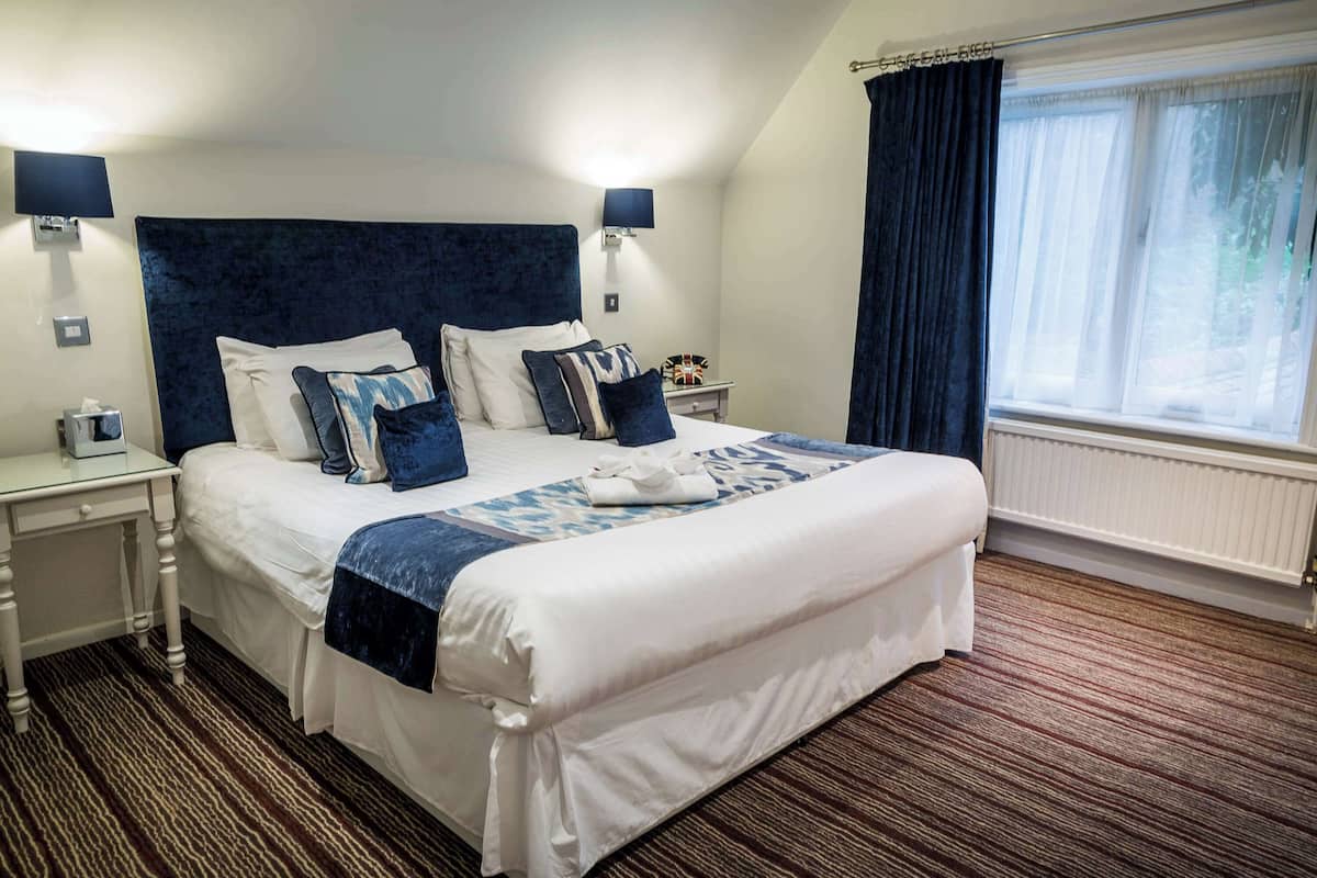 A hotel room with a large bed, two bedside tables, a nightstand, a window with curtains, and a wall-mounted TV.