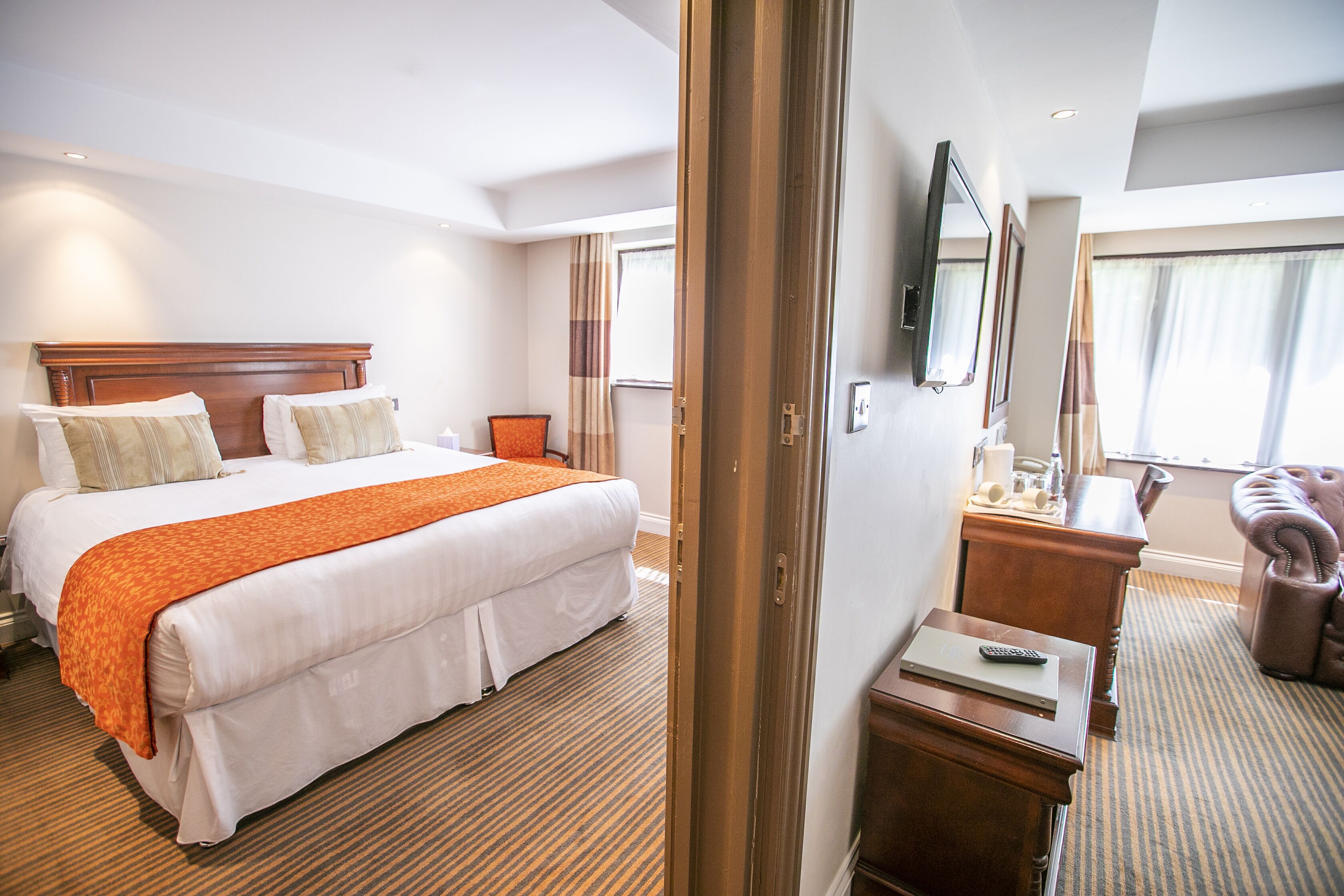 A hotel room with a large bed, a desk with a chair, a TV, and a leather armchair.