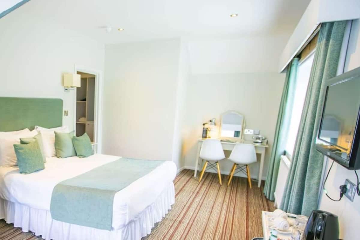 A hotel room with a bed, a desk with a chair, a television, and a wardrobe.