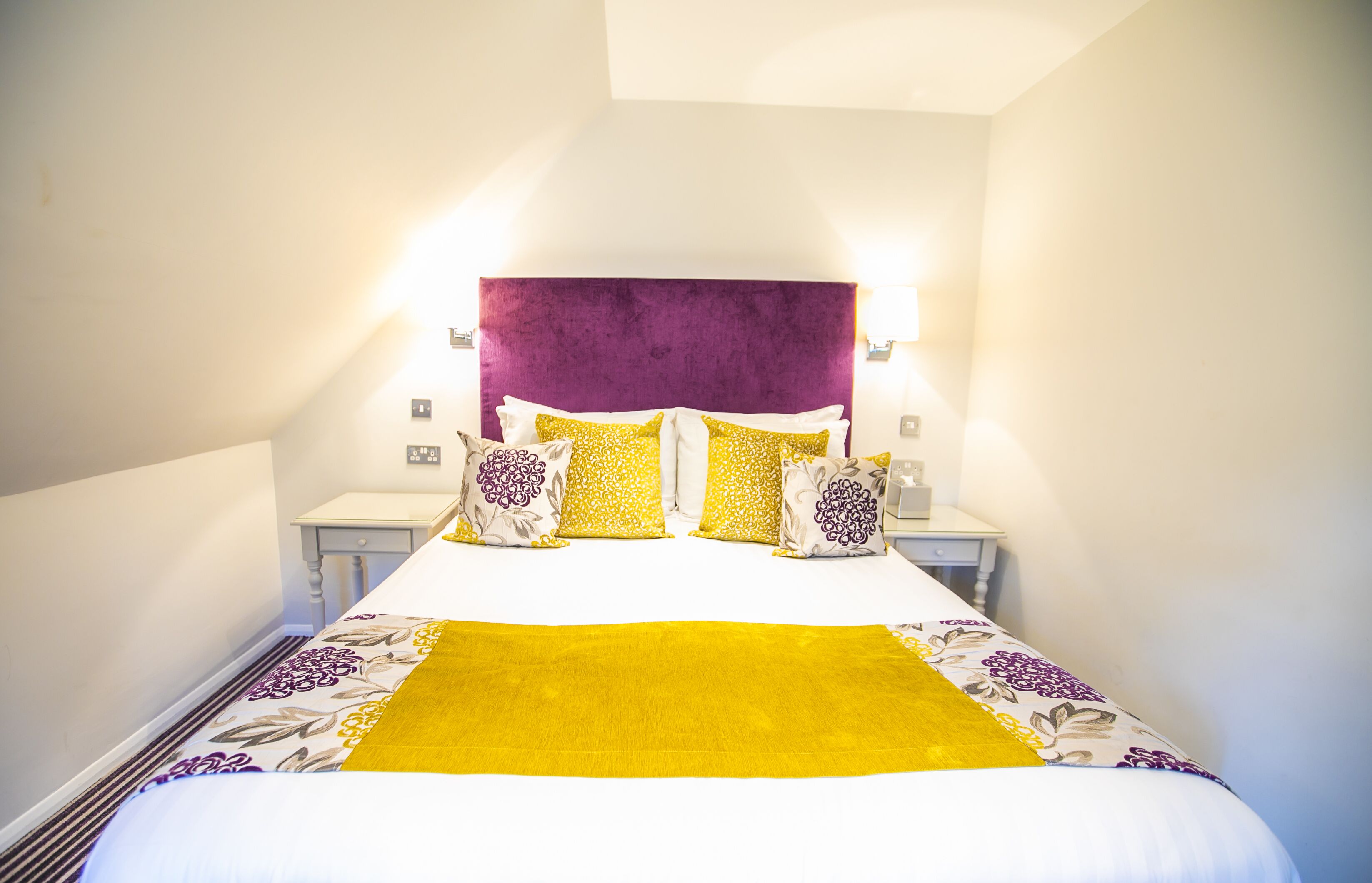 A neatly made bed with a purple headboard, white and yellow pillows, and a yellow throw blanket.