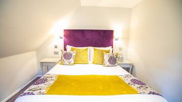 A neatly made bed with a purple headboard, white and yellow pillows, and a yellow throw blanket.