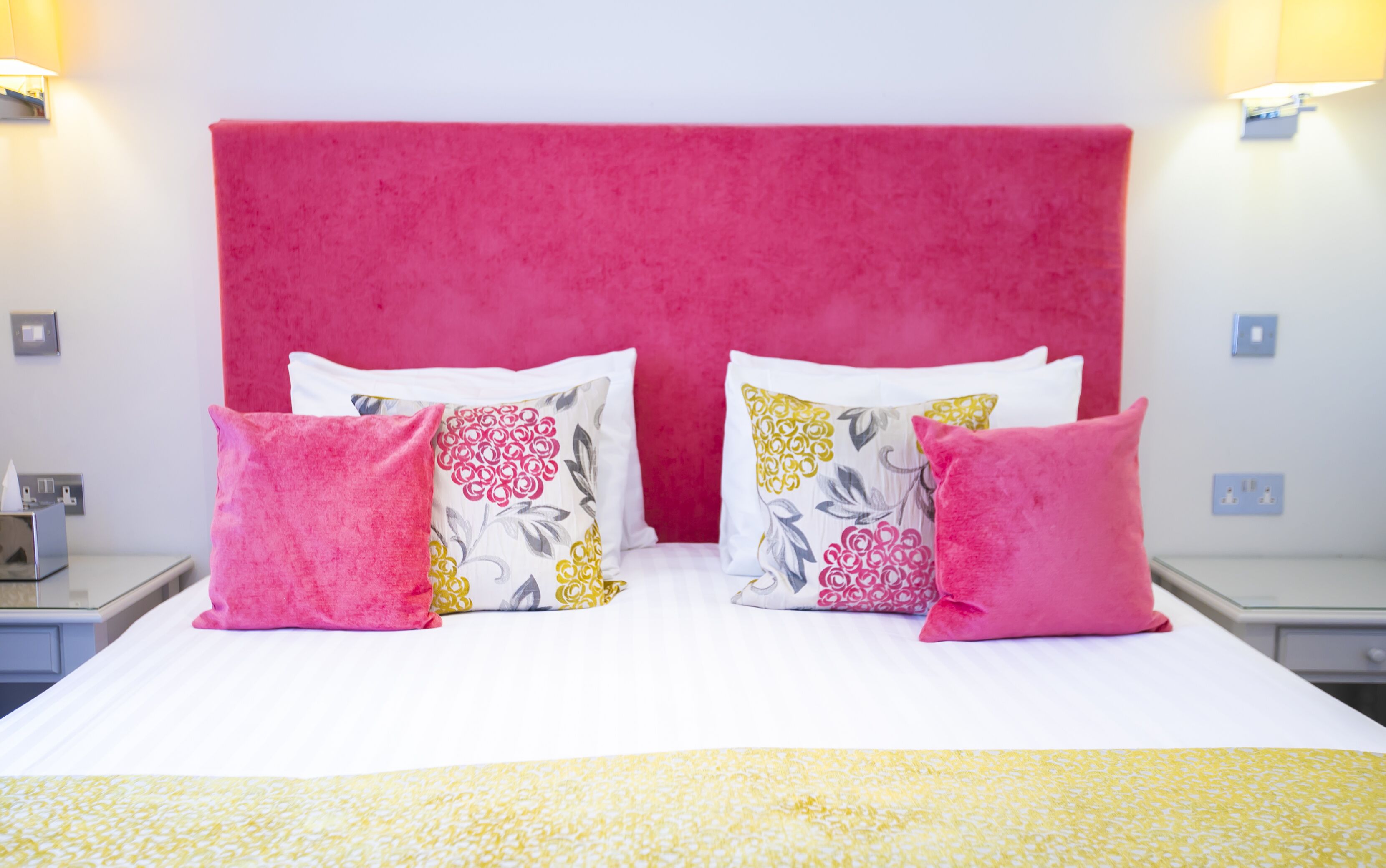 A bed with a pink headboard, white bedding, and decorative pillows with floral patterns.