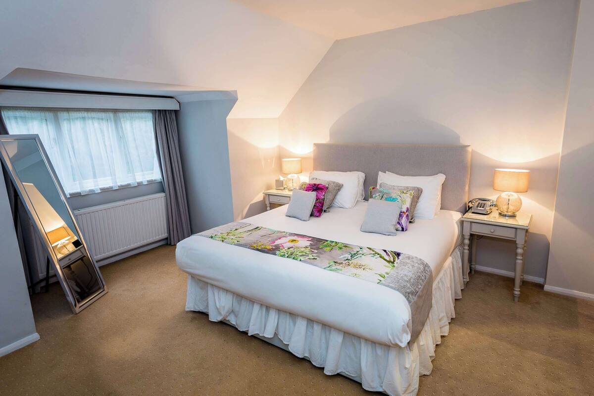 A neatly arranged hotel room with a large bed, bedside lamps, a bedside telephone, and a window with curtains.