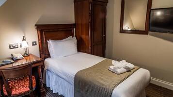 A hotel room with a bed, a wooden wardrobe, a desk with a lamp, a telephone, and a television.
