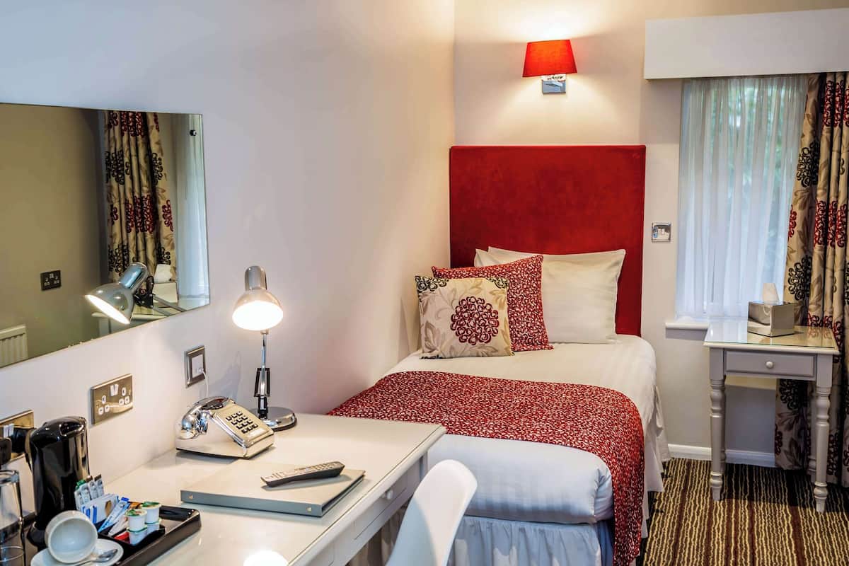 A hotel room with a bed, bedside table, lamp, phone, and a desk with a mirror.