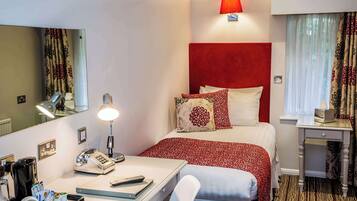 A hotel room with a bed, bedside table, lamp, phone, and a desk with a mirror.