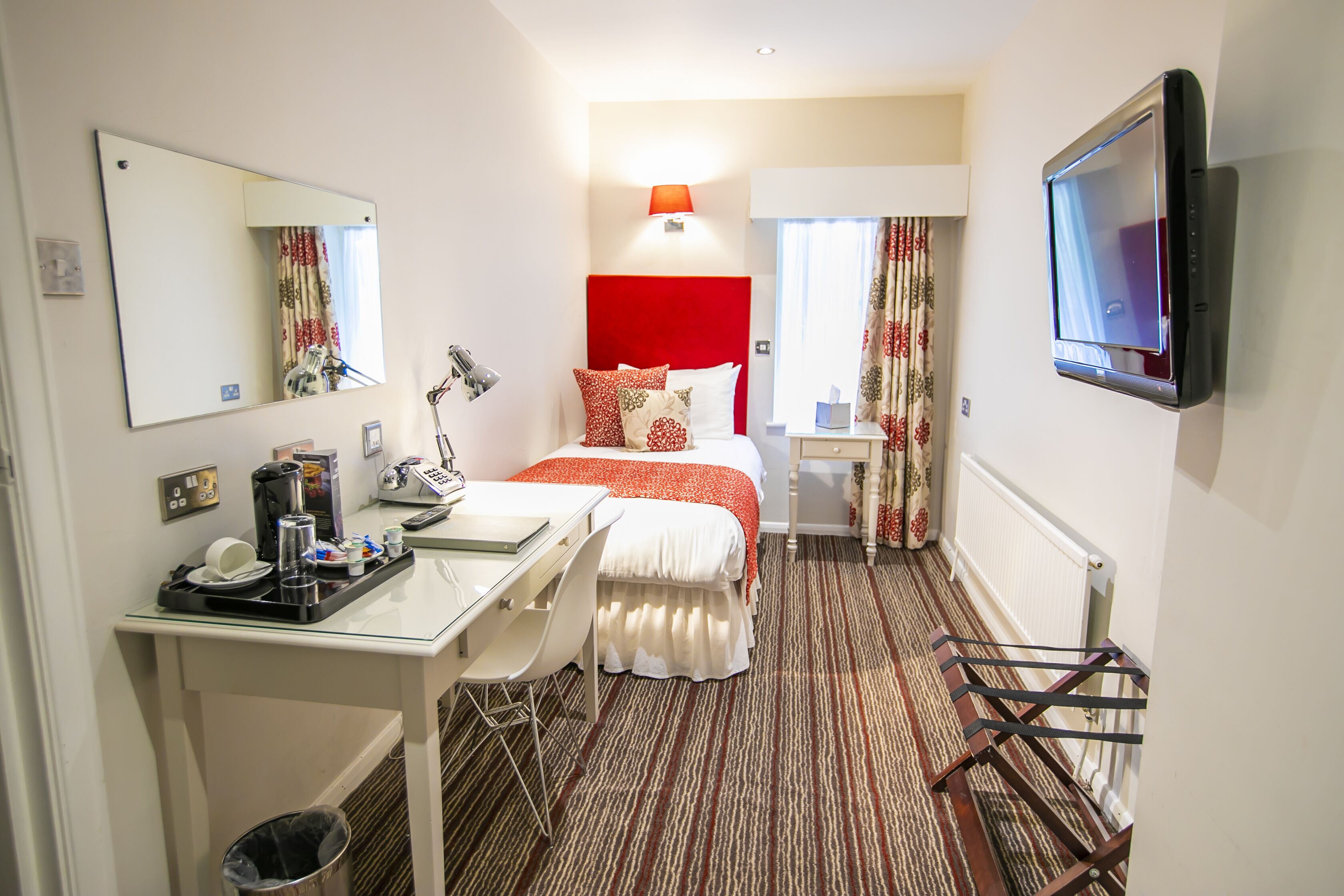 A hotel room with a bed, a desk with a chair, a TV mounted on the wall, and a radiator.