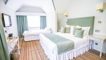 A hotel room with two beds, a small desk, a mirror, a window with curtains, and a radiator.
