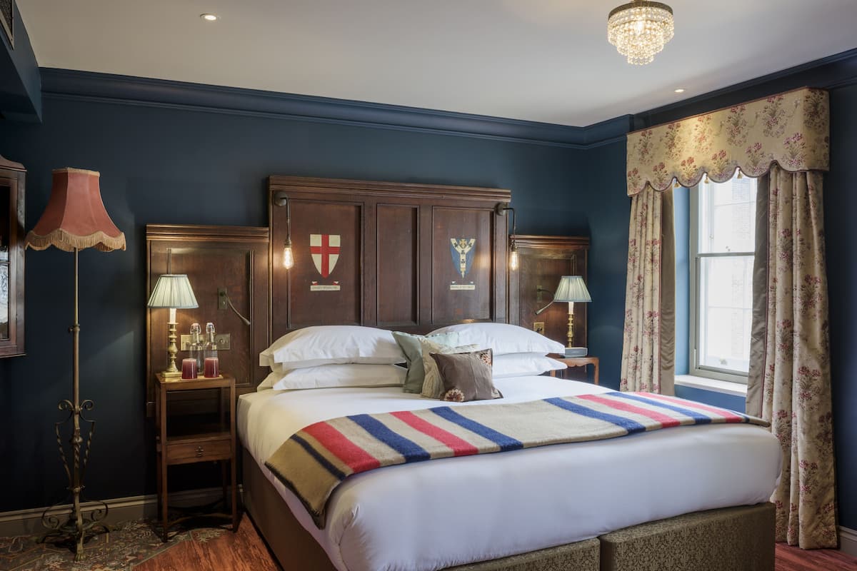 A bedroom with a large bed, two bedside tables with lamps, a chandelier, and a window with curtains.