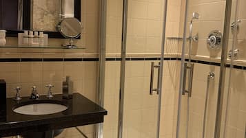 A modern bathroom with a glass-enclosed shower, a black sink, and a mirror above it.