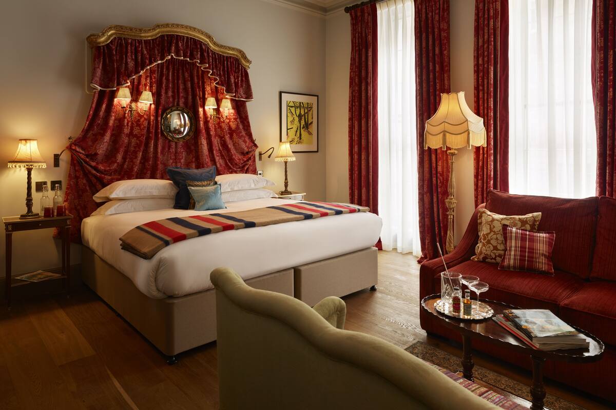 A hotel room with a large bed, red curtains, a sofa, and a coffee table with a magazine and a glass.