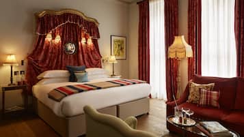 A hotel room with a large bed, red curtains, a sofa, and a coffee table with a magazine and a glass.