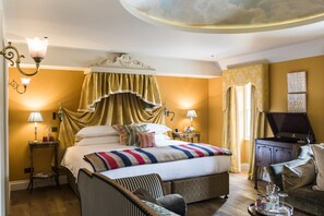Une chambre élégamment aménagée, dotée d’un grand lit, d’une coiffeuse avec miroir, d’une télévision et d’un piano.