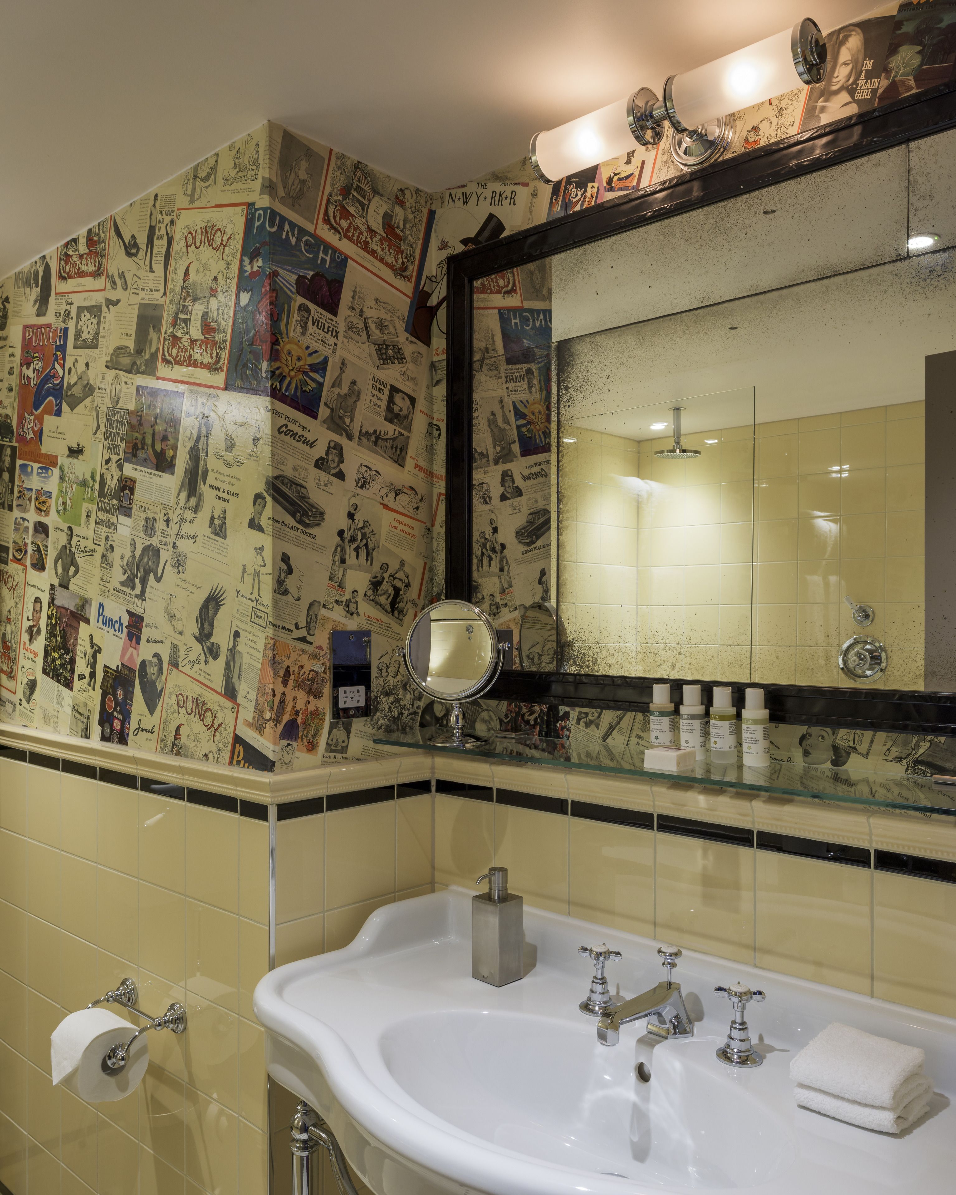 A bathroom with a sink, mirror, and wall covered in vintage posters.