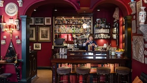 Zona de bar con un camarero, estantes de licores y taburetes.