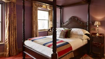 A four-poster bed with a wooden frame and a canopy, a red carpet, and a patterned rug.