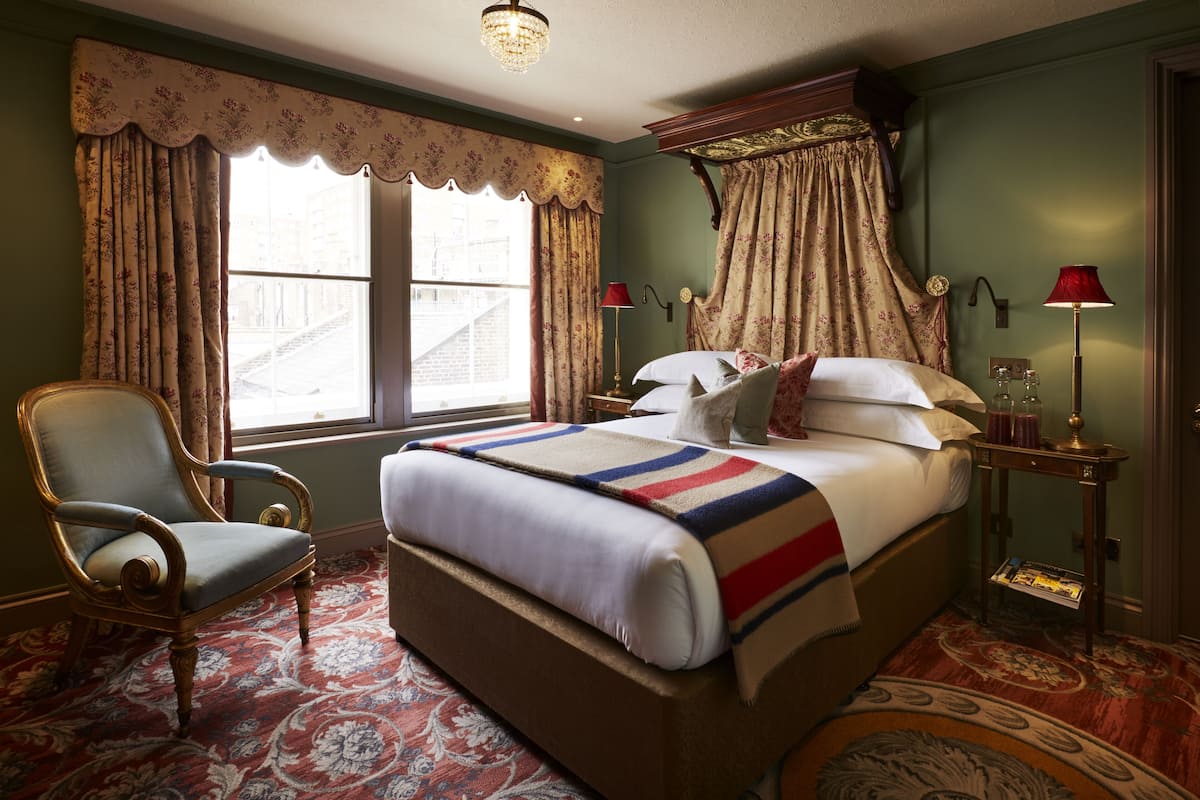 A traditional bedroom with a large bed, a chair, and a window with curtains.