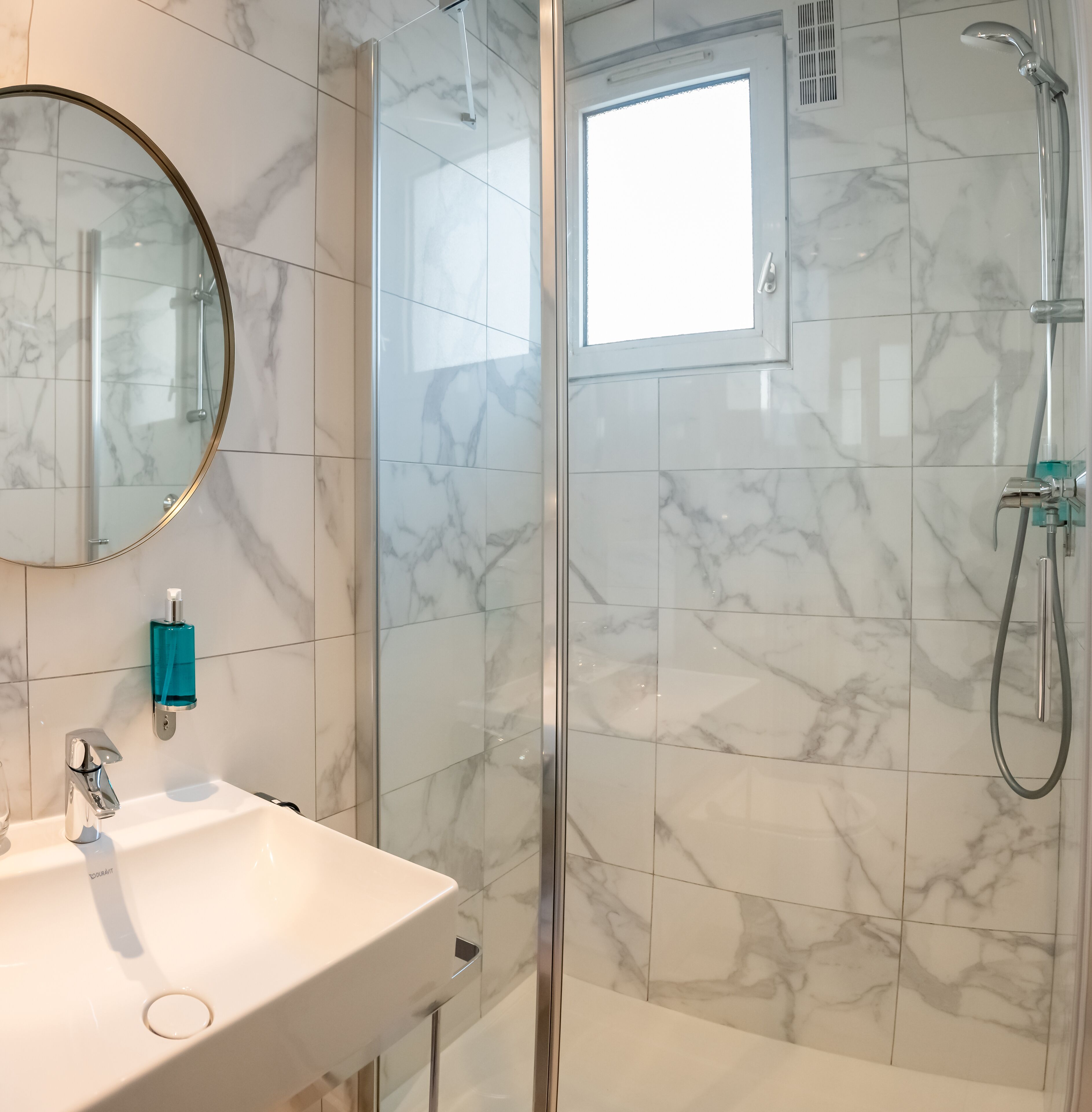 Une salle de bain avec une douche à parois de verre, un lavabo avec un miroir et des carreaux de marbre.