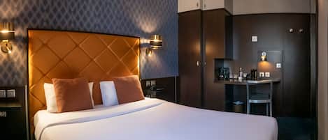 Una habitación de hotel con una cama grande, cabecera, lámparas de noche, un escritorio con silla y un espejo.