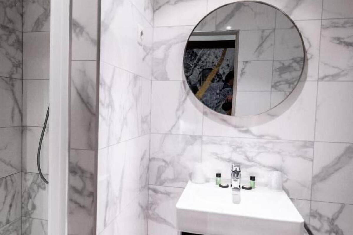 A bathroom with a marble wall, a round mirror, and a white sink with two bottles.
