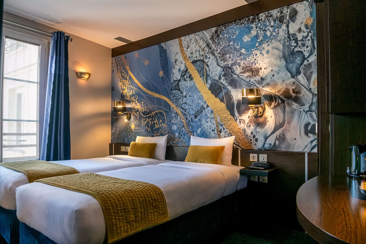 A hotel room with two beds, a large abstract painting on the wall, and a wooden side table.