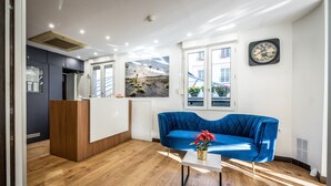 A modern reception area with a wooden reception desk, a blue sofa, and a clock on the wall. - Hôtel du Parc (Paris)