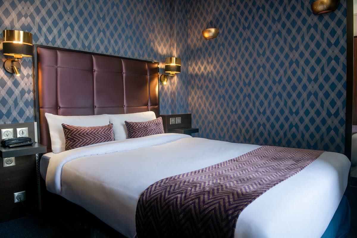 A neatly made bed with a patterned throw, a headboard with a tufted design, and two wall-mounted lamps on either side.