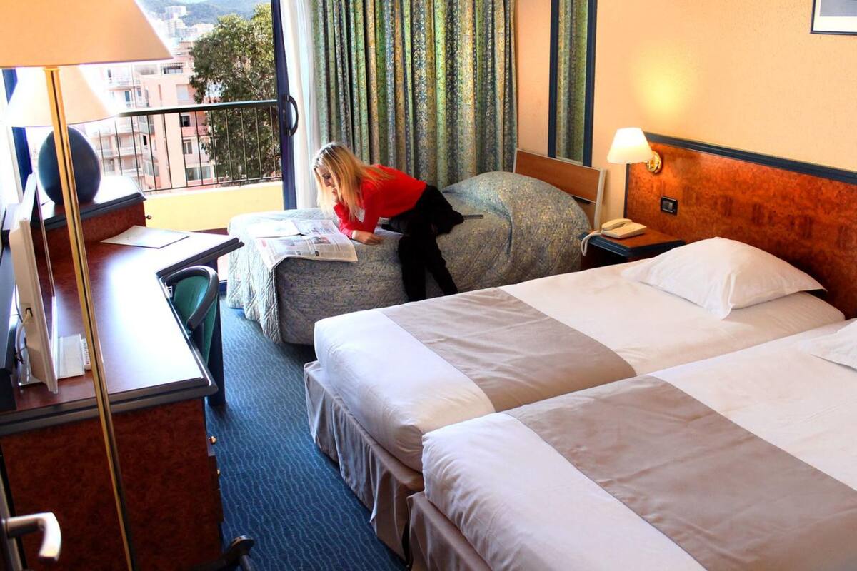 A hotel room with two beds, a desk with a computer, and a window with curtains.