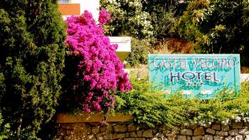 Segnaletica dell'Hotel Castel Vecchio immersa nel verde e circondata da piante fiorite.