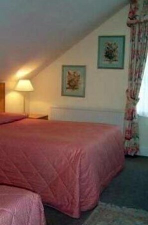A bedroom with a large bed, a bedside table, a lamp, and two framed pictures on the wall. - Hayesthorpe Hotel (South Croydon)