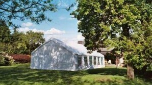 A small, white, single-story house with a gabled roof and a porch, surrounded by lush green grass and trees. - Hayesthorpe Hotel (South Croydon)