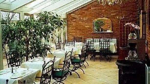 A dining area with tables and chairs, a brick wall, and a large plant. - Hayesthorpe Hotel (South Croydon)