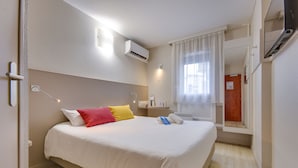A hotel room with a bed, a bedside table, an air conditioner, a window with curtains, and a door. - Brit Hotel Lille Centre (Lille)