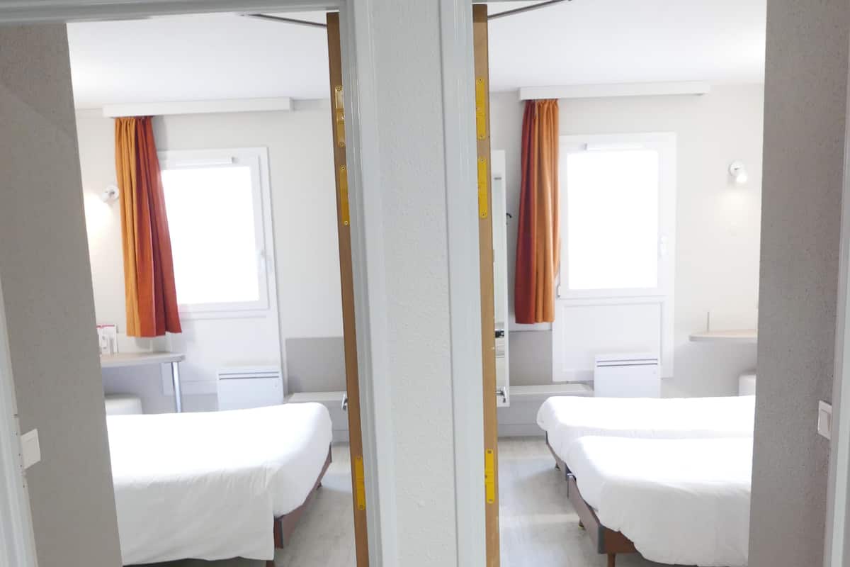 A hotel room with two beds, a window with curtains, and a bathroom visible through an open door.