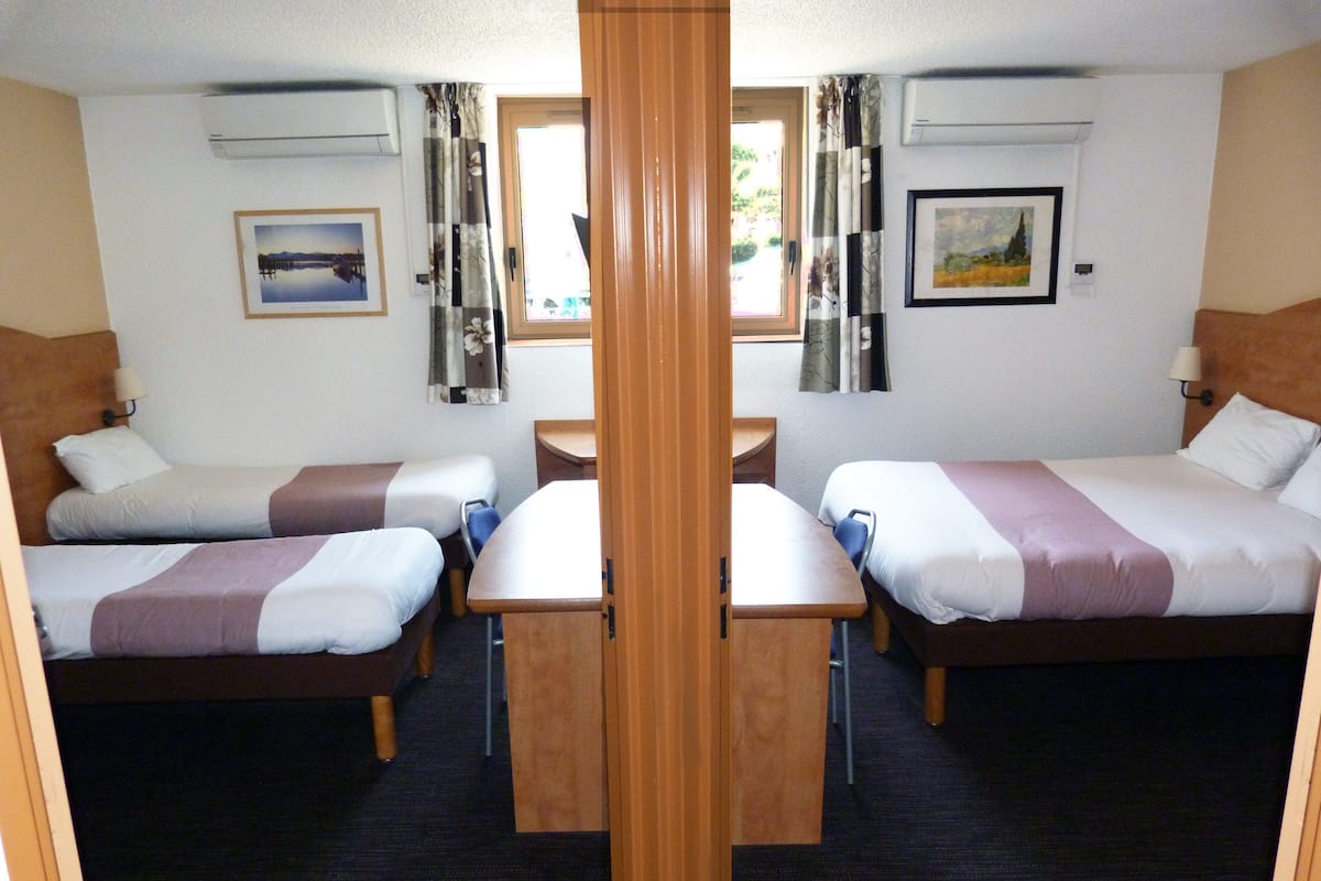 Ein Hotelzimmer mit zwei Einzelbetten, einem kleinen Tisch, einem Stuhl und einem Fenster mit Vorhängen.