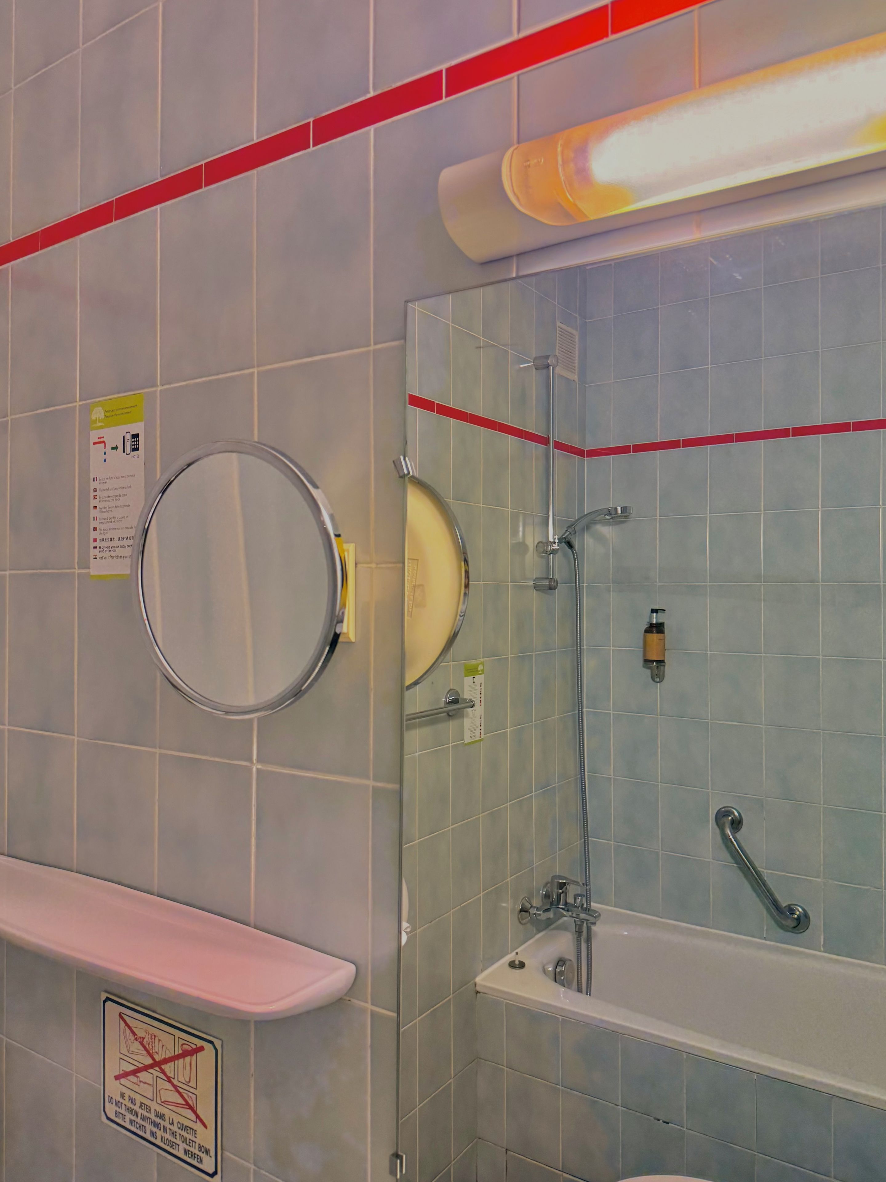 Et badeværelse med bruser, håndvask og toilet. Der er en håndtørrer og en sæbedispenser på væggen.